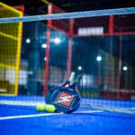 Blue padel court with racket and yellow balls, emphasizing dynamic sports vibe indoors.