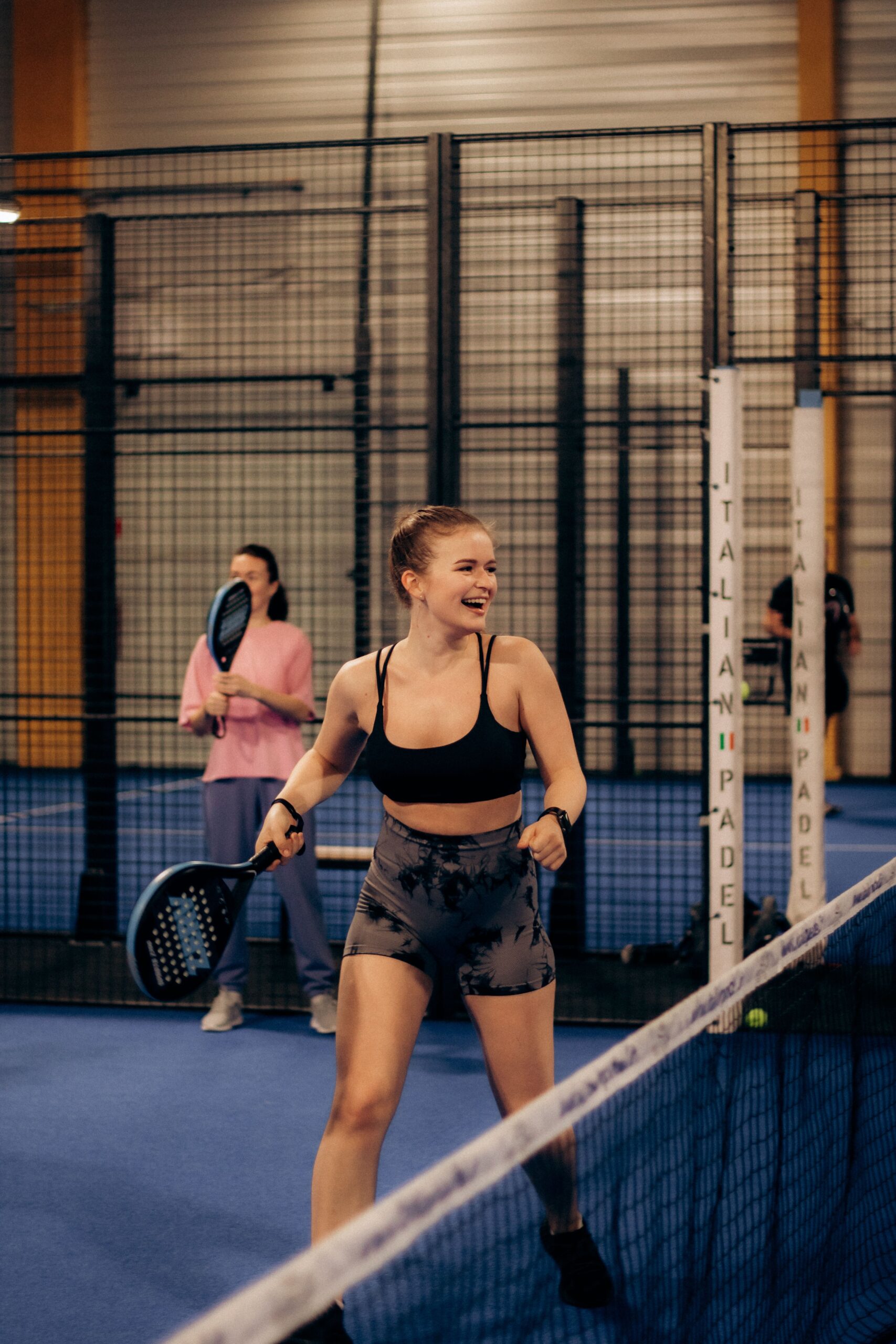 Two women enjoying a game of padel tennis in an indoor sports facility.