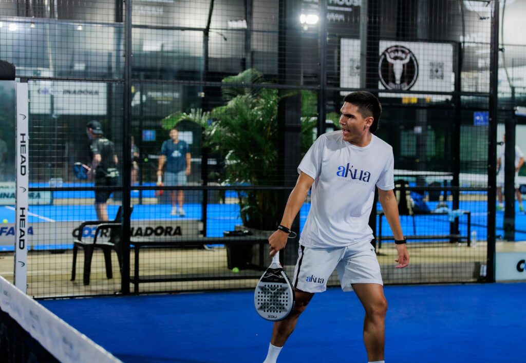 Energetic padel tennis player at indoor court mid-match.